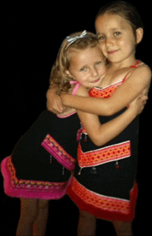 two little girls hugging each other with one wearing a black dress