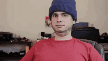 a man wearing a red t-shirt and a blue beanie is sitting in a chair .