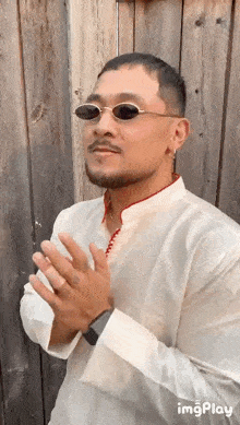 a man wearing sunglasses and a white shirt is standing in front of a wooden fence
