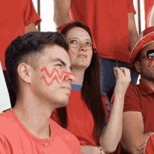 a group of people in red shirts are sitting in a stadium and one of them has a w painted on his face .