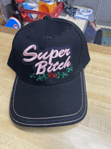 a black baseball cap with the words super bitch embroidered on it