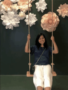 a woman sits on a swing in front of flowers