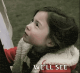 a little girl is looking up with the words `` we 'll see '' written above her .