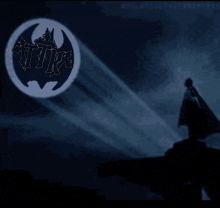 a silhouette of a man stands in front of a bat logo
