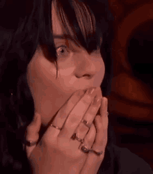 a close up of a woman with rings on her hands covering her mouth .