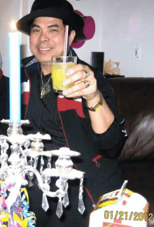 a man holds a glass of orange juice with a straw in front of a candle holder