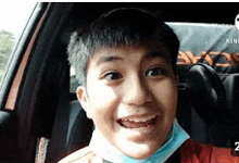 a young boy wearing a mask is sitting in the back seat of a car .