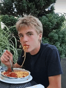 a young man is sitting at a table eating spaghetti with a fork and spoon .