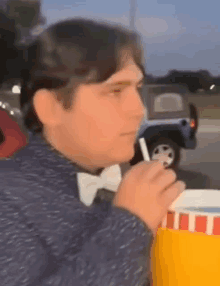 a man wearing a bow tie is drinking from a cup with a straw in his mouth .