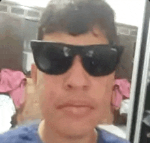 a man wearing sunglasses is taking a selfie in a bathroom .