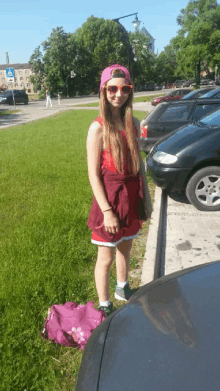 a girl wearing a pink hat and sunglasses stands next to a car