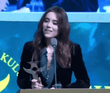 a woman is sitting at a podium holding a trophy and speaking into a microphone .