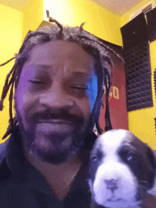 a man with dreadlocks is holding a small puppy in front of a yellow wall with a red sign that says 40