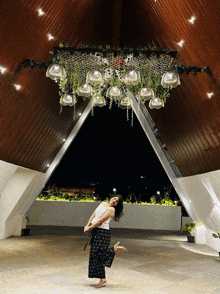 a woman stands in front of a ceiling with flowers hanging from it