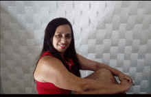 a woman in a red tank top is sitting in front of a white wall