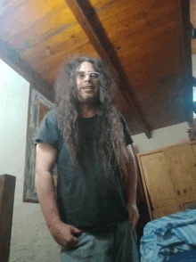 a man with long hair wearing glasses and a black shirt stands in front of a wooden ceiling