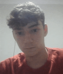 a young man with curly hair is wearing a red shirt and headphones .