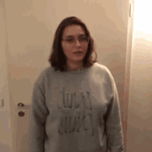 a woman wearing glasses and a grey sweater that says ' duer ' on it