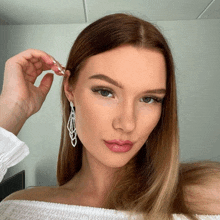 a woman wearing a white off the shoulder top and earrings looks at the camera