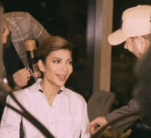 a woman in a white shirt is sitting in front of a microphone while a man in a baseball cap talks to her .