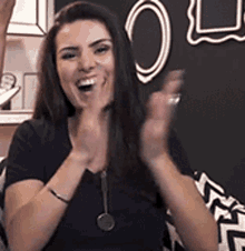 a woman is sitting on a couch with her hands in the air and a chalkboard in the background .