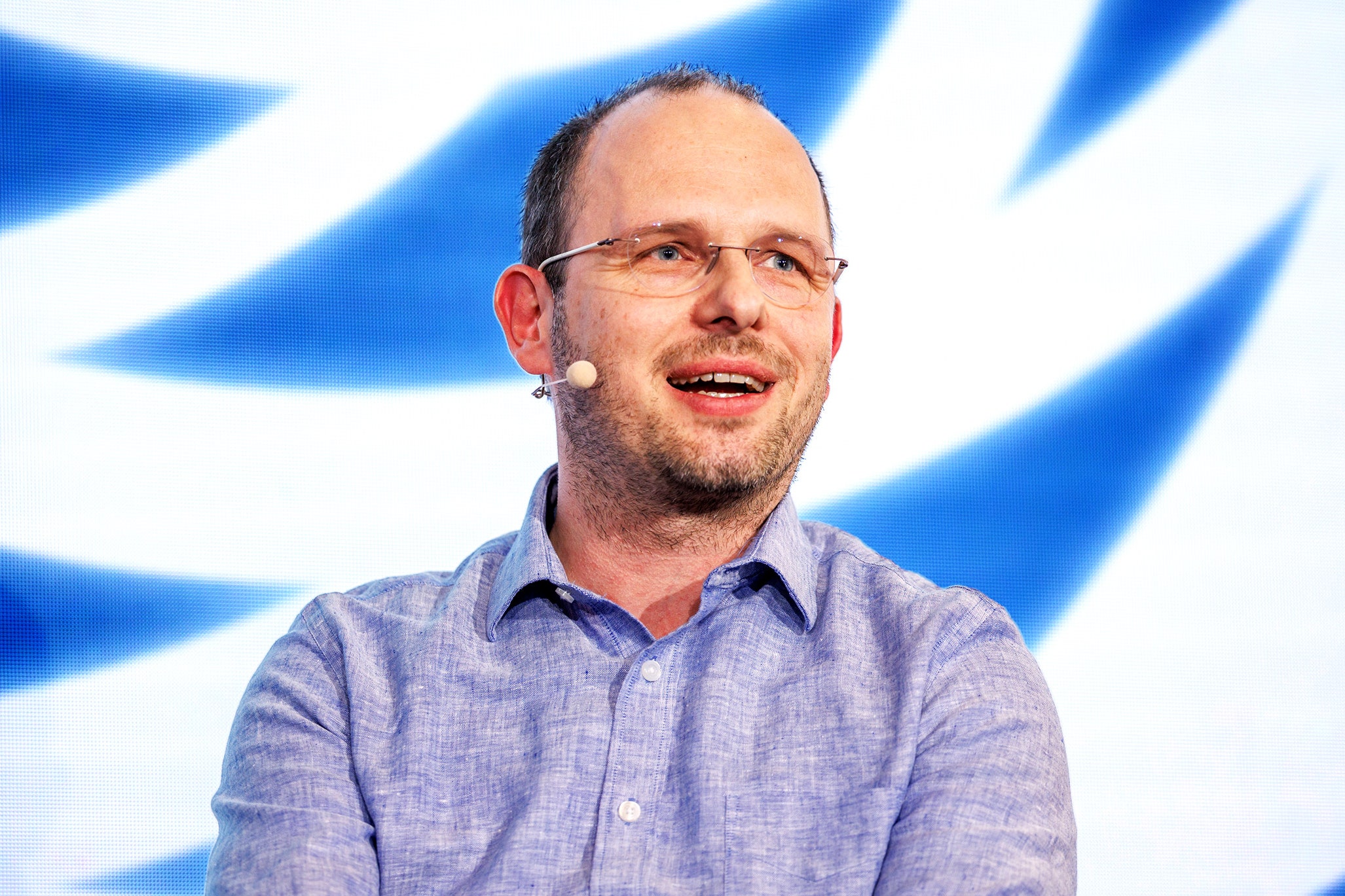 Person speaking in front of a large screen with a blue and white graphic on it