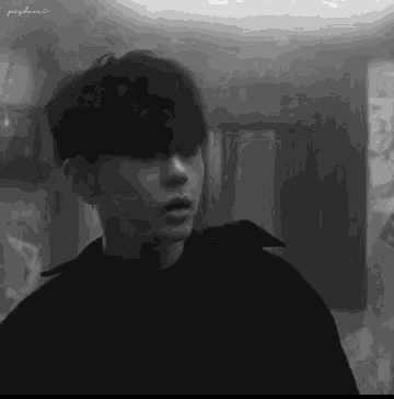 a black and white photo of a young man standing in a room looking at the camera .