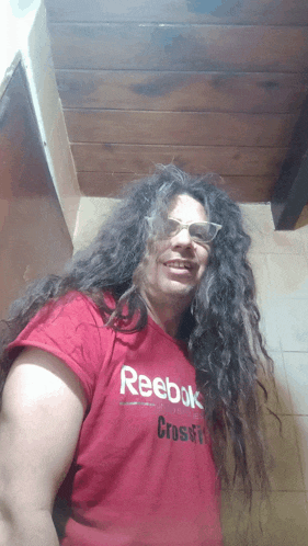 a woman with long curly hair wearing a red reebok crossfit shirt