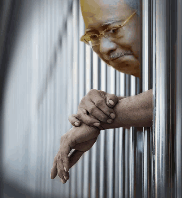 a man with glasses and a mustache looks out of a prison cell