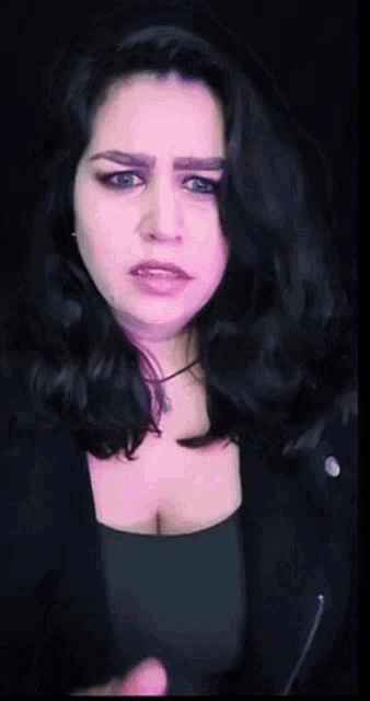 a woman with dark hair and blue eyes is making a face