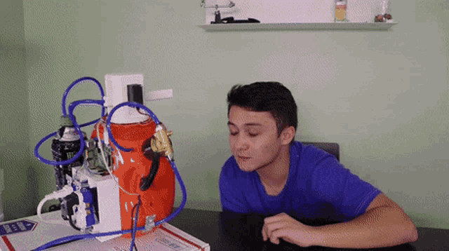 a man in a blue shirt is sitting at a table in front of a machine that has a coca cola bottle in it