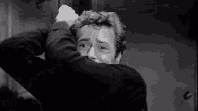 a black and white photo of a man covering his face with his arms .