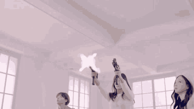 three women are holding up guns in a room with a white ceiling .