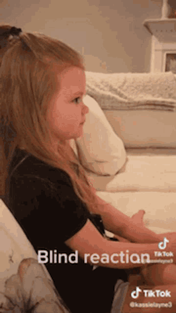 a little girl is sitting on a couch with blind reaction written on the bottom