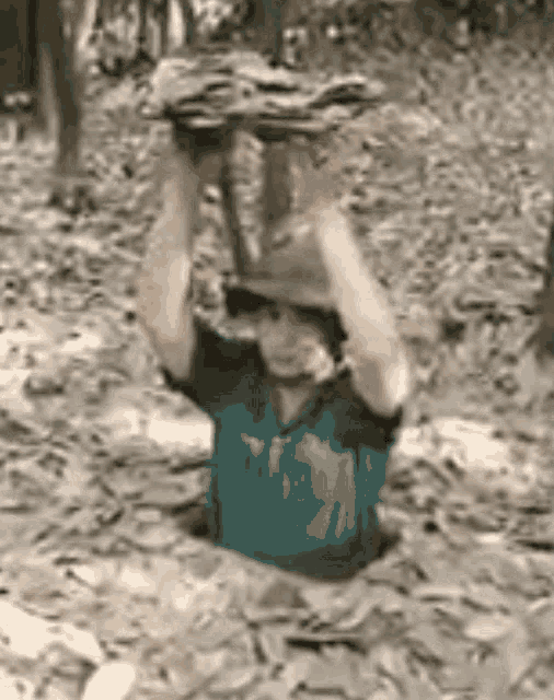 a man is holding a large rock over his head while crawling out of a hole in the dirt .