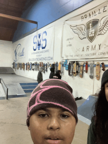 a boy wearing a pink beanie stands in front of a sign that says braille