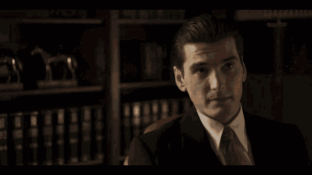 a man in a suit and tie sitting in front of a bookshelf