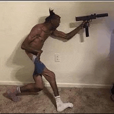 a shirtless man is kneeling down and holding a gun in a room .