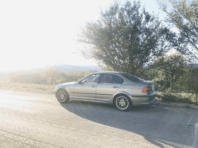 a silver bmw is parked on the side of a road