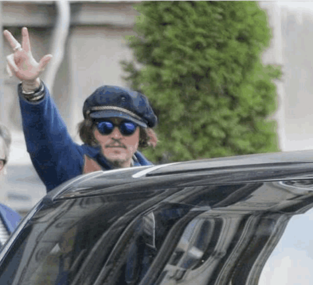 a man wearing sunglasses and a hat is waving from a car window