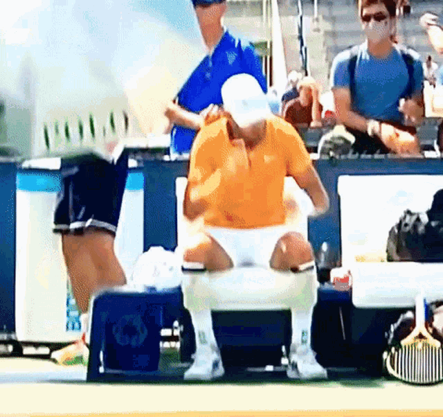 a man in an orange shirt sits on a bench in front of a recycling box