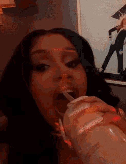 a woman with long white nails is drinking from a bottle with a straw in her mouth .