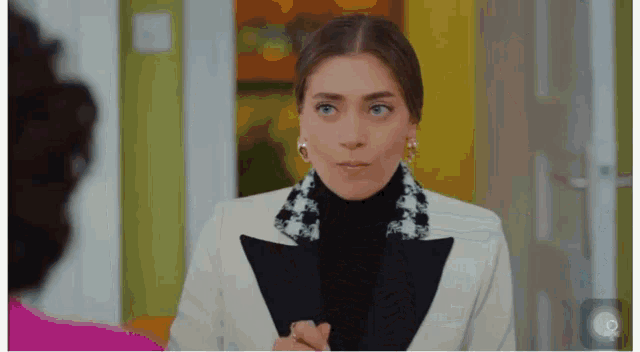 a woman in a white suit and black turtleneck is holding a clipboard .