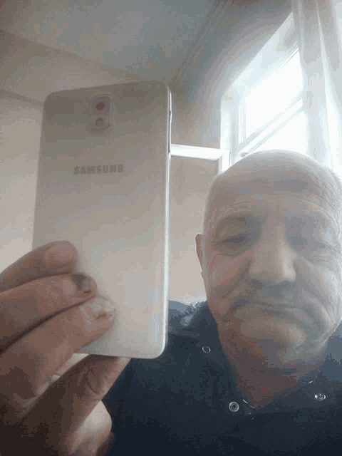 a man holds up a samsung phone in front of a window