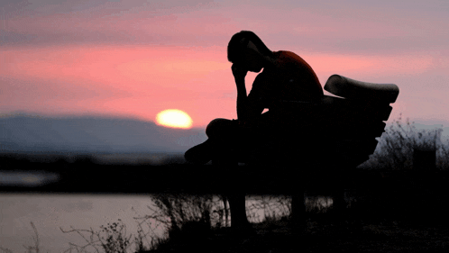 a silhouette of a person sitting on a bench with the sun behind them