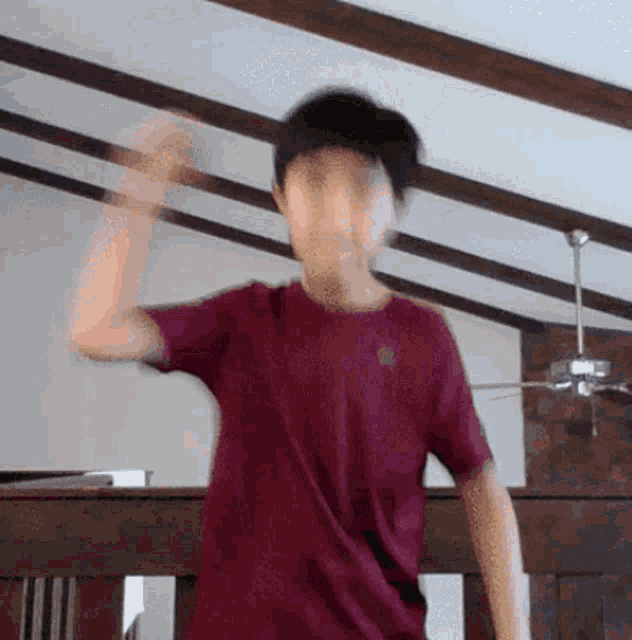 a man in a maroon shirt is dancing in a room with a ceiling fan