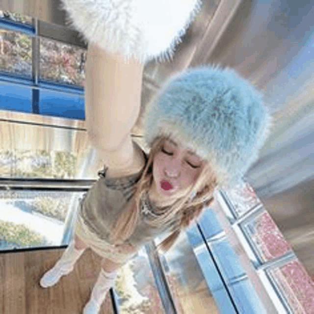 a woman wearing a fur hat is standing in front of a window with her arms up .