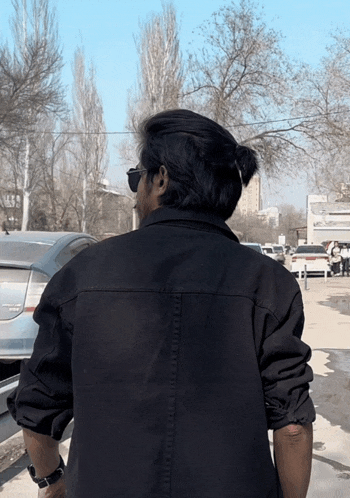 a man wearing sunglasses and a black jacket stands in front of a car