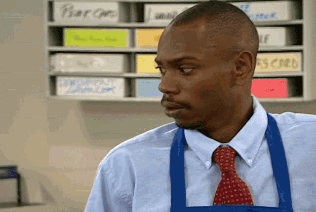 a man wearing a blue apron and tie stands in front of a shelf with boxes labeled ' pear '