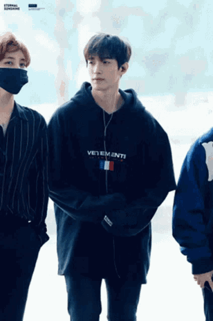 a man wearing a vetements hoodie stands next to another man